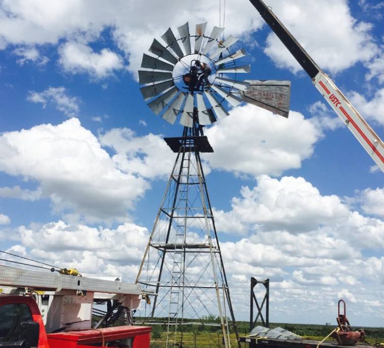 windmill with a crane attached to it, standing in a field